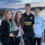 Four teenagers standing on a boat deck with water and islands in the background during sunset. They are all looking at the camera, with two boys on the right and two girls on the left.