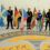 Seven students stand in a line holding various national flags on a floor with "Anderson High School" written on it.