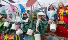 Group of people in ocean-themed costumes holding buckets stand on a decorated float.