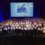 Large group of award recipients on stage holding certificates at the Saltire Awards Ceremony 2024. A projector screen behind them displays the event's logo and name.