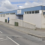 A white and blue building with a sign reading "Shetland Recreational Trust, Shetland Bowls Centre" on a partially cloudy day. Cars are driving on the street in front of it.