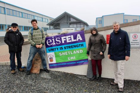 Four individuals stand outside a building holding a banner that reads, “eis FELA - Unity Is Strength - Shetland UHI - Further Education Lecturers' Association.