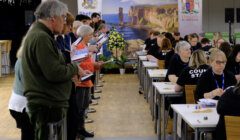 People are gathered in a room, some seated and some standing, engaged in counting activities. A backdrop displays images of the Orkney Islands with "Orkney" written at the top.