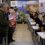 People are gathered in a room, some seated and some standing, engaged in counting activities. A backdrop displays images of the Orkney Islands with "Orkney" written at the top.