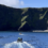 Two small boats with people in high-visibility jackets navigate a calm body of water near a rugged, grassy cliff coastline under a clear blue sky.