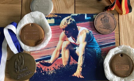 A photo of an athlete surrounded by three Paralympic medals: two bronzes from the Barcelona 1992 Paralympics, a silver medal, and a bronze medal from another event. A German ribbon is also displayed.