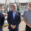 Three men standing outdoors in front of a marina with boats and buildings in the background, all smiling and facing the camera.