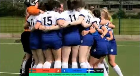 A women's field hockey team in white and blue uniforms huddles in celebration. A scoreboard shows Okeey 2 and Shebad 4 with the date 27-07-24 and text indicating the Lady Harberton Cup.