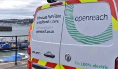 A van with "Openreach" and "I'm 100% electric" signage, promoting "Ultrafast Full Fibre broadband," is parked near a harbor with boats in the background.