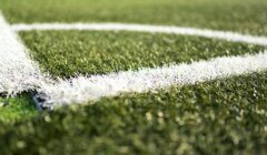 Close-up of the white line on synthetic green grass of a sports field, possibly a soccer or football field, with the blurred background.