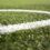 Close-up of the white line on synthetic green grass of a sports field, possibly a soccer or football field, with the blurred background.