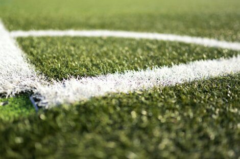 Close-up of the white line on synthetic green grass of a sports field, possibly a soccer or football field, with the blurred background.