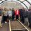 A group of people stands inside a greenhouse structure with raised garden beds filled with soil. They seem to be posing for the photo.