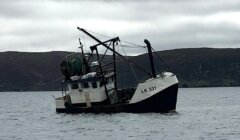 A fishing boat labeled "LK 331" floating in a body of water with hilly terrain in the background under a cloudy sky.