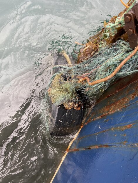 A ship's propeller entangled with fishing nets and ropes submerged in water.