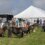 People and ponies gathered in a field near a large white tent, participating in what appears to be a small equestrian event or show.