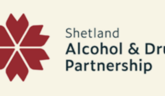 Logo of Shetland Alcohol & Drug Partnership featuring a red geometric flower design to the left of the organization's name in text.