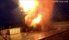 A large explosion with flames and smoke captured on surveillance camera at a facility with storage containers and fencing on August 19, 2024, at 20:14:52.