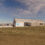 A single-story building with a "Statkraft" logo on the facade is situated in an open field under a partly cloudy sky. Several parked cars are visible in the background.