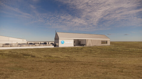 A single-story building with a "Statkraft" logo on the facade is situated in an open field under a partly cloudy sky. Several parked cars are visible in the background.