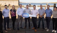 A group of nine people are standing outdoors near a waterfront, holding signs with the ESB logo and the text "Energy for generations." Buildings and boats are visible in the background.