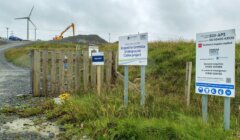 Construction site with signs for the Kiergoed to Gremista Underground Cables project. Wind turbines and construction equipment visible in the background.