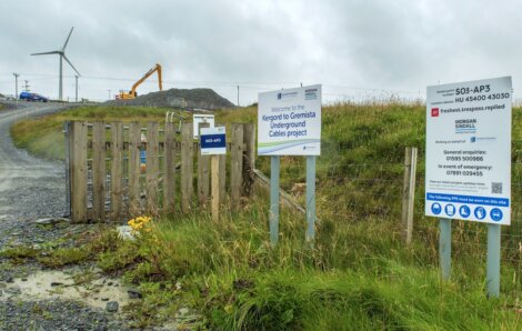 Construction site with signs for the Kiergoed to Gremista Underground Cables project. Wind turbines and construction equipment visible in the background.