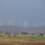 Wind turbines on a hill overlooking a rural landscape with scattered houses and green fields under a cloudy sky.