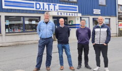 Four men stand together outside the entrance of a building with a sign reading "D.I.T.T.