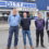 Four men stand together outside the entrance of a building with a sign reading "D.I.T.T.