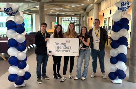 Five young individuals stand holding a banner that reads "Young Islanders Network" between two balloon columns with "Big Ideas" signs at the top in an indoor setting.