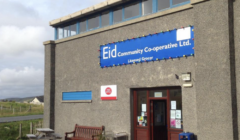 Storefront of Eid Community Co-operative Ltd. A bench and picnic table are outside. Several signs are displayed near the entrance, including one for a licensed grocer.