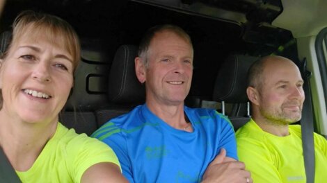 Three people in bright athletic shirts sitting in a car, smiling and looking ahead.