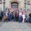 A large group of people of various ages posing together in front of a stone building with a wooden door.