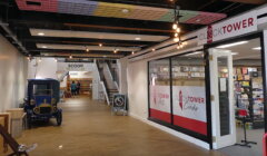 A modern indoor market with a toyshop named Clocktower, an ice cream parlor called Scoop, and a vintage car display. Brightly lit with decorative ceiling elements and wooden flooring.