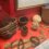 A display case showcases various woven baskets, balls of natural fibers, and bundles of raw materials. The items are arranged on a red surface.