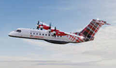 A Logan Air aircraft with tartan tail design is mid-flight against a partly cloudy sky. The plane's propellers are in motion.