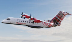 A Logan Air aircraft with tartan tail design is mid-flight against a partly cloudy sky. The plane's propellers are in motion.