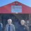 Four men stand in front of the Walls Community Fire Station, a red building with an open door. A sign above the entrance reads "Scottish Fire and Rescue Service.