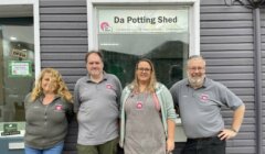 Four people standing in front of a grey building with a sign that reads "Da Potting Shed." They all wear grey shirts with matching logos.