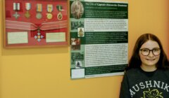 A girl stands next to a display of medals and an informational board about Captain Alexander Bremner's life.