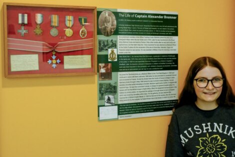 A girl stands next to a display of medals and an informational board about Captain Alexander Bremner's life.