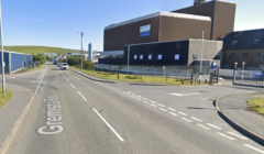 Street intersection with Gremista Road and a nearby industrial building in the background on a clear day.