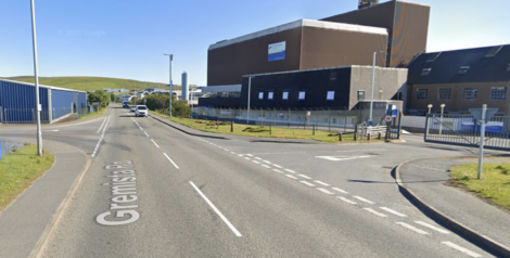 Street intersection with Gremista Road and a nearby industrial building in the background on a clear day.