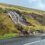 A hillside with visible erosion shows streams of water and mud flowing down towards a roadside.