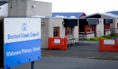 Sign reading "Shetland Islands Council Whiteness Primary School" in front of a school building with red fencing and blue trim.