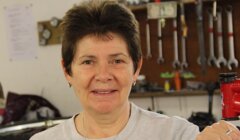 A person smiling in a workshop, tools and equipment visible in the background.