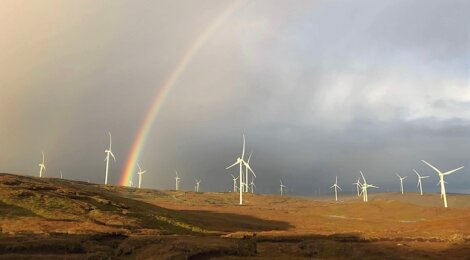 Wind turbines spread across a hilly landscape with a rainbow in the background.