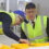 Two people wearing high-visibility vests and caps examine bins filled with ice cubes, inside an industrial setting.