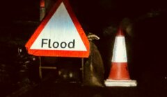 Traffic cones and a flood warning sign are placed on a dark street as a caution for flooding.